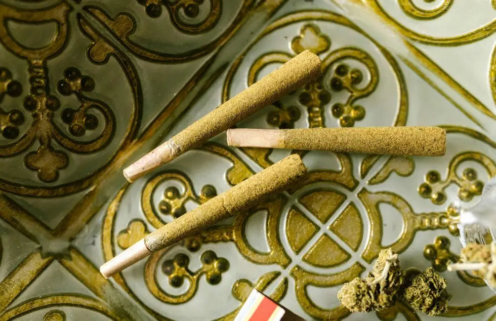 Drei Joint-Varianten mit braunem Rolling Paper und weißen Tips auf Ornament-Oberfläche